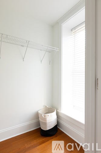 A white wall with a clothes hanger and a white bucket on the floor.