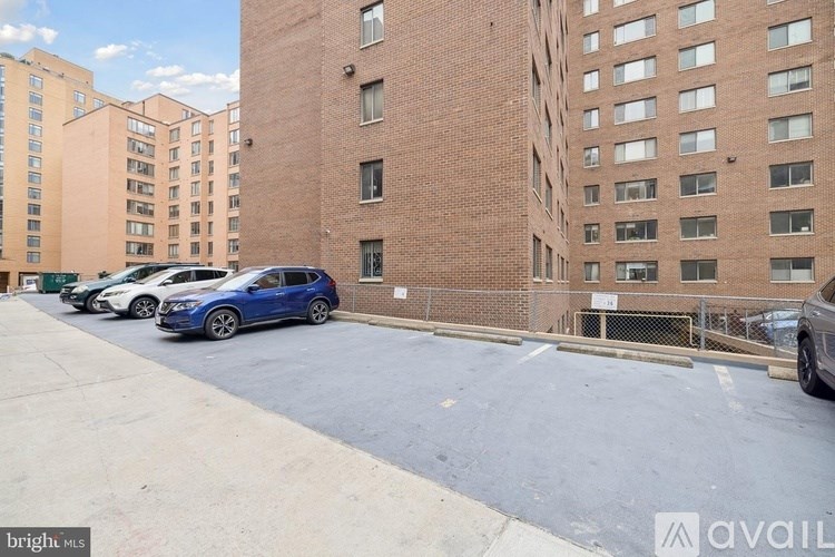 A parking lot with a blue car and a tall brick building in the background.