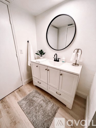 A white bathroom with a round mirror and a white cabinet.