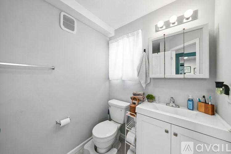 A white bathroom with a toilet, sink, mirror, and a towel hanging on the towel rack.