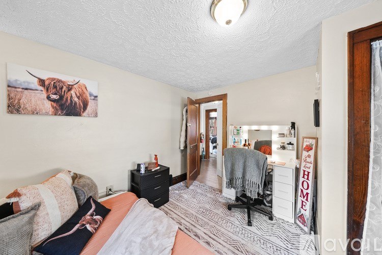 A bedroom with a bed, a chair, and a picture of a cow on the wall.