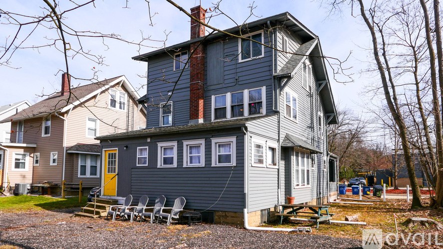 A house with a grey exterior and a yellow door is surrounded by bare trees.