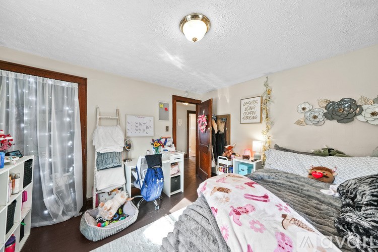 A bedroom with a bed, dresser, and a window with sheer curtains.