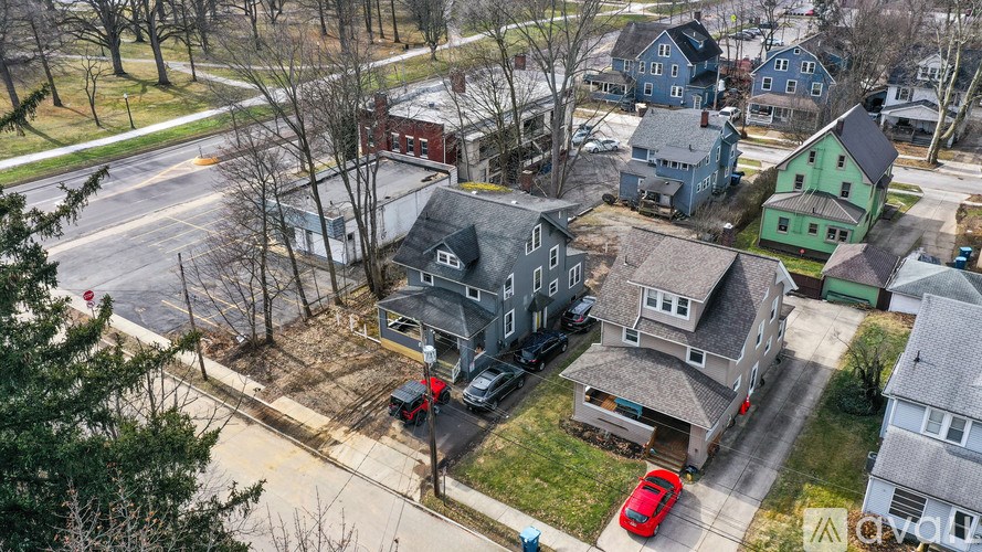 A red car is parked in front of a grey house.