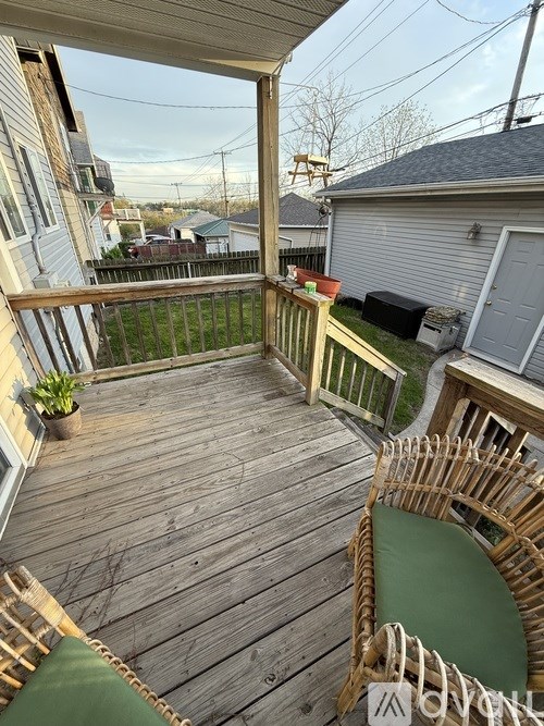 A wooden deck with a green cushion and a woven chair.