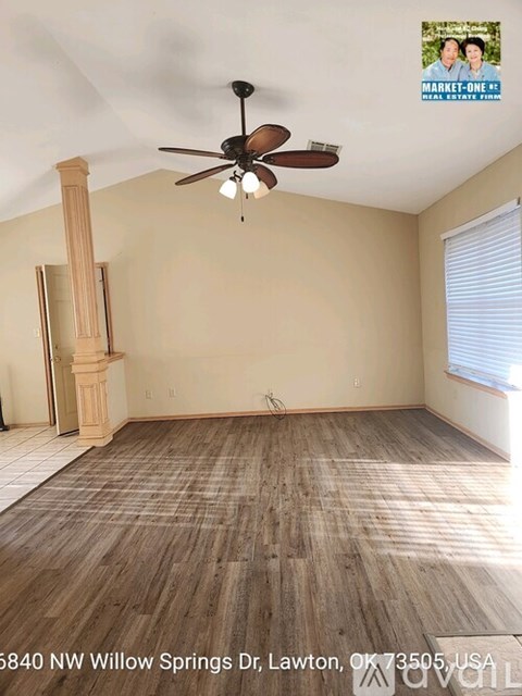 A room with a ceiling fan and light, hardwood floors, and a large window with blinds.