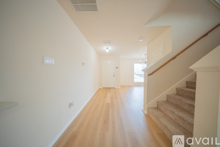 A hallway with wooden floors and a staircase on the right side.