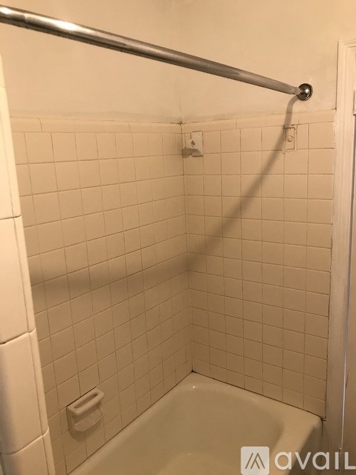 A white tiled shower with a metal grab bar.