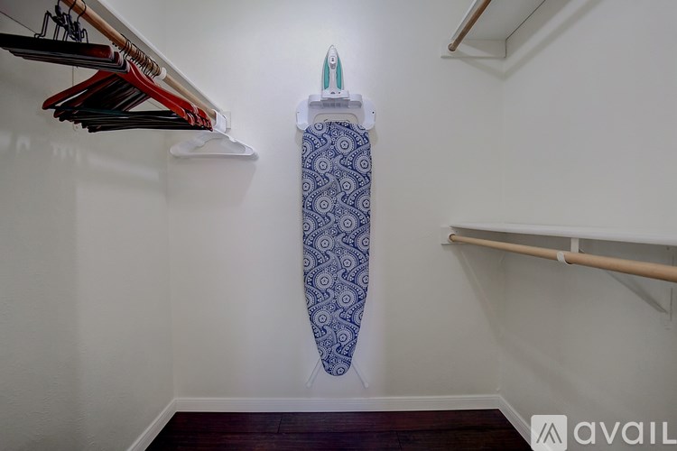 A blue and white patterned umbrella is hanging on a wall next to a white ironing board.