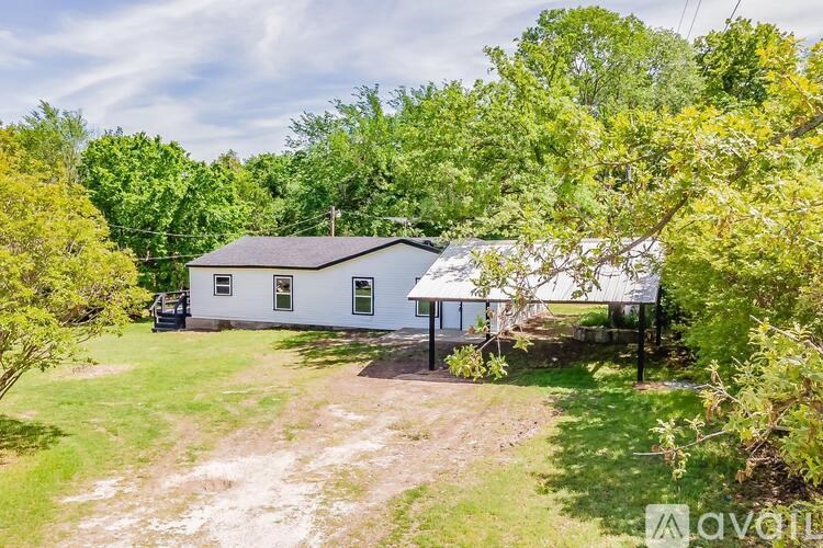 A white house with a porch surrounded by green trees.