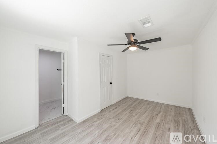 A room with a ceiling fan and light, two doors, and a wooden floor.