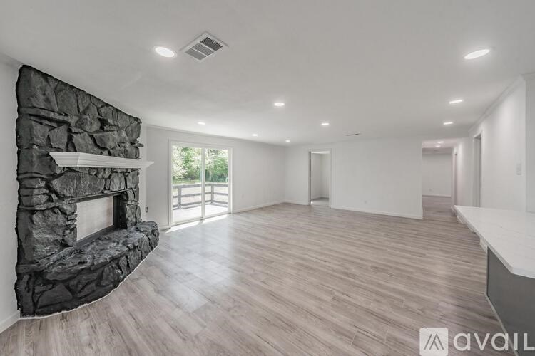 A spacious room with a stone fireplace and wooden flooring.