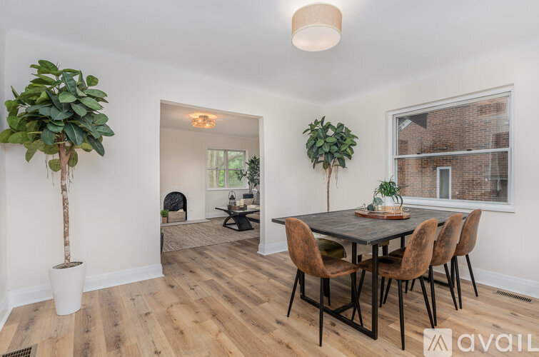 A room with a wooden table and chairs, a potted plant, and a window with a view of a brick building outside.
