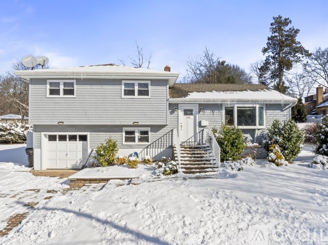 A house with a grey roof and white garage door is surrounded by snow.