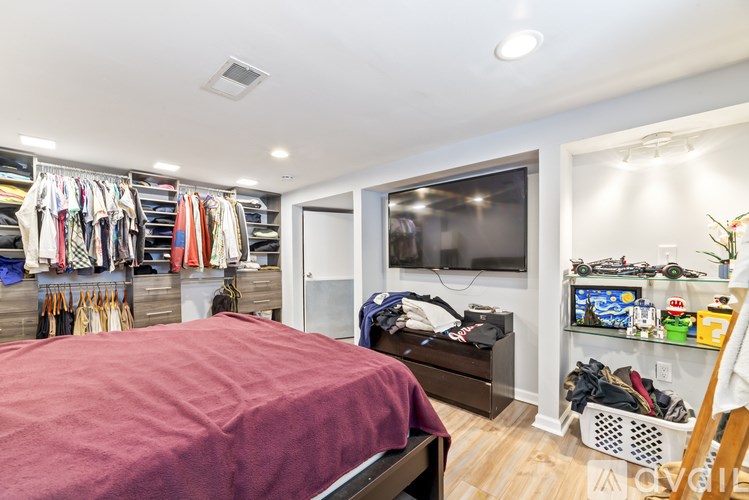 A bedroom with a bed, a TV, and a closet full of clothes.