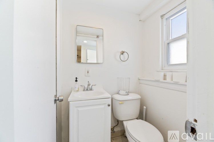 A white bathroom with a toilet, sink, mirror, and a window.