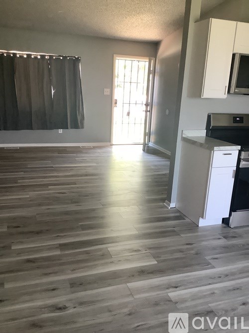 A room with wooden flooring and a kitchen area with white cabinets.