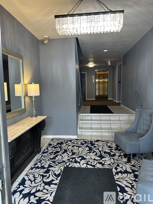 A hallway with a chandelier, a mirror, and a bench.