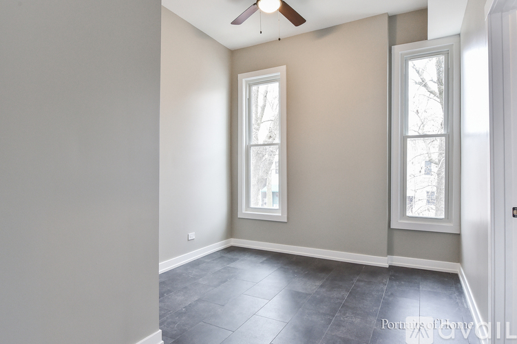 A room with a ceiling fan and two windows.