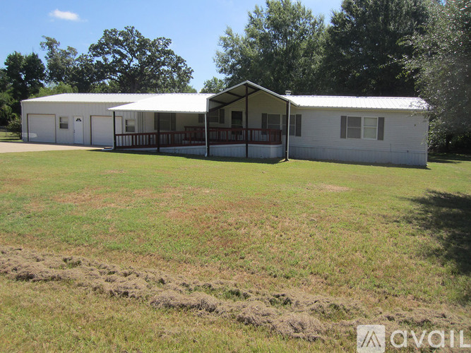 A white house with a porch and a covered patio is surrounded by a grassy field.