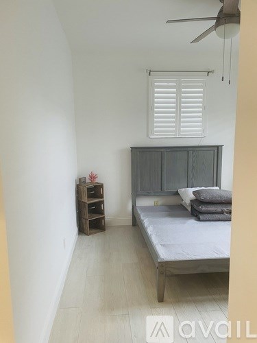 A bedroom with a bed, a window with blinds, and a wooden nightstand.
