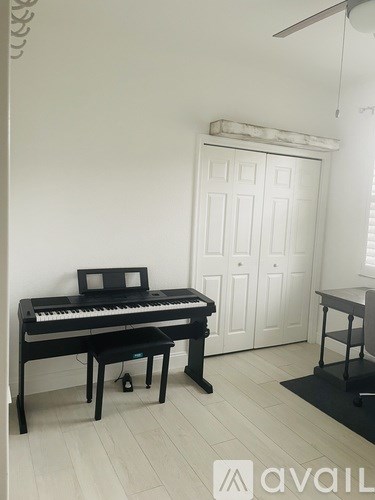 A black piano with a bench in front of a white door.