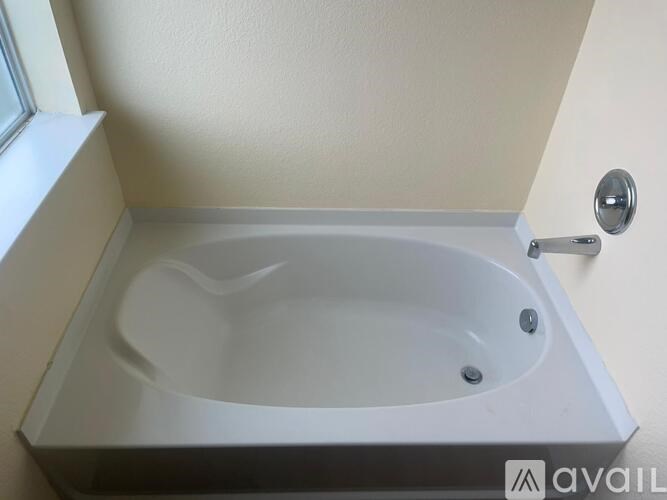 A white bathtub is installed in a bathroom with a window above it.