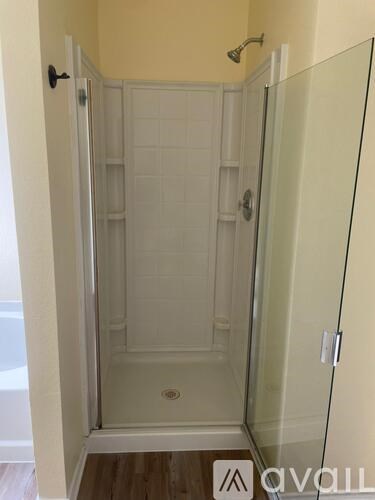 A glass shower stall with a white door and a black handle.