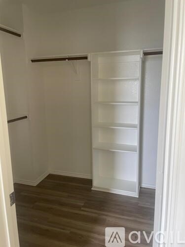 A white shelving unit with multiple shelves is in a room with wooden flooring.