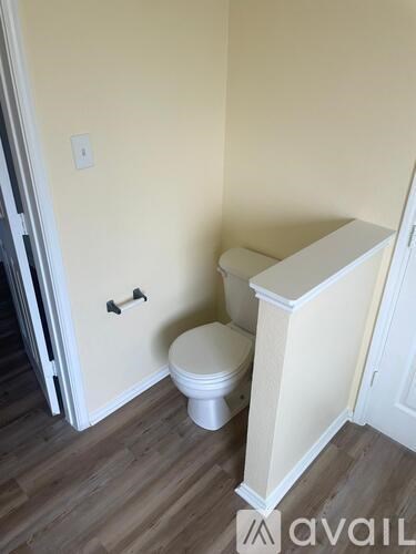A white toilet sits in a small bathroom with wooden floors.
