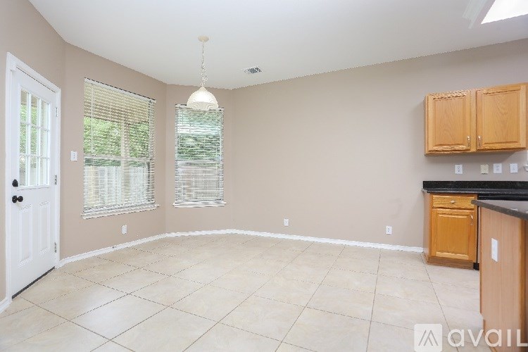 A room with a white door, a window with blinds, and a kitchenette with wooden cabinets.