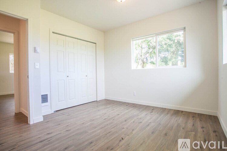 A room with a white door and a window with a view of trees outside.