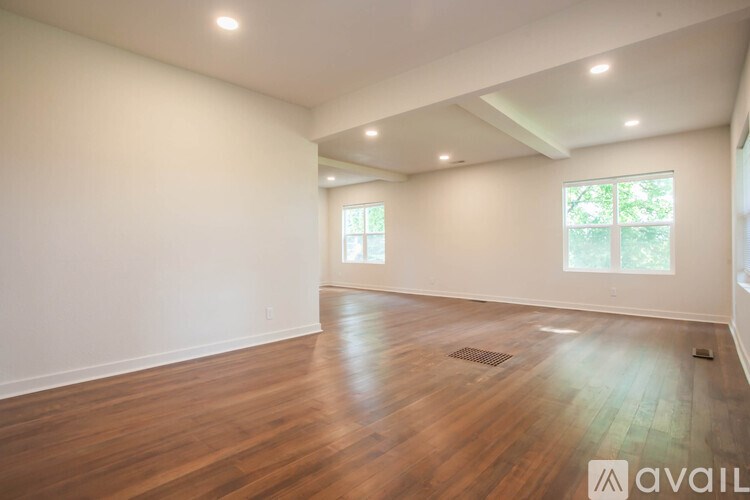 A spacious room with wooden floors and two windows.