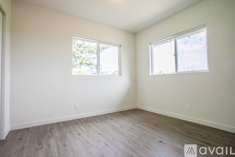 A room with wooden flooring and two windows.
