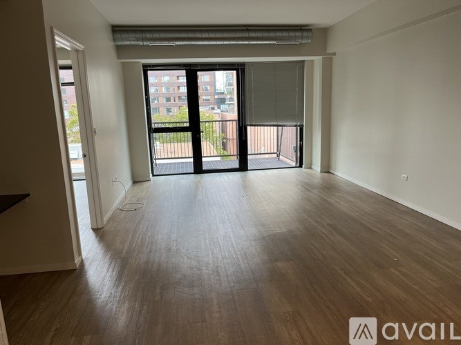A spacious room with wooden flooring and a view of a balcony with a railing.