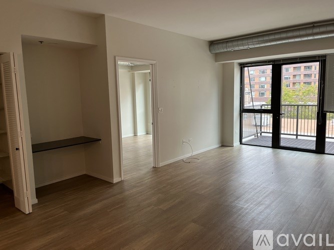 A spacious room with wooden flooring and a sliding glass door leading to a balcony.