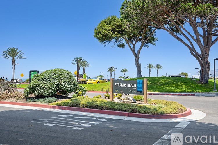 A sign for Strandits Beach is in front of a tree and a parking lot.
