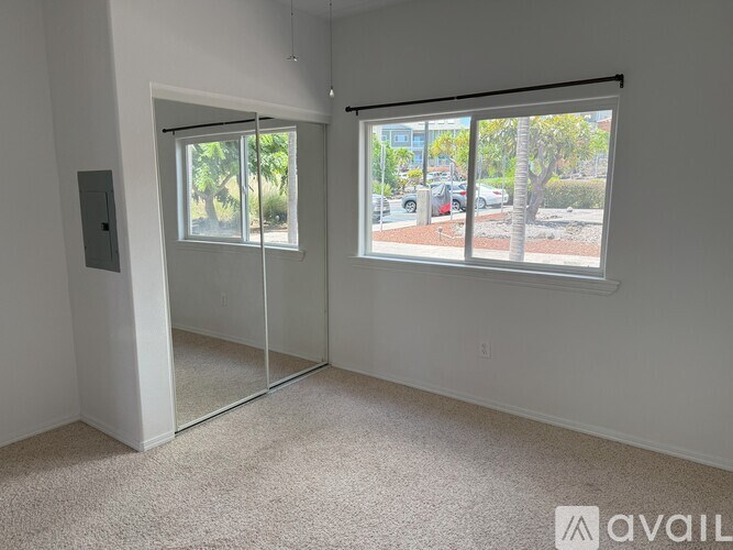 A room with a carpeted floor, a white wall, and a window with a view of the outside.