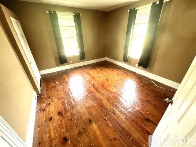 A room with wooden floors and a window with green curtains.