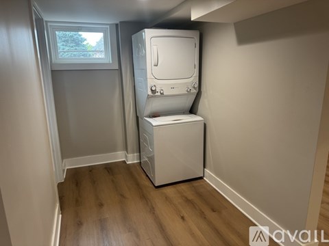 A white tankless water heater in a room with wooden flooring and a window.