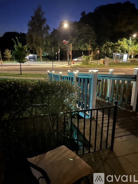 A balcony with a bench and a railing overlooking a street at night.