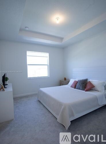 A bedroom with a white bed and a window.