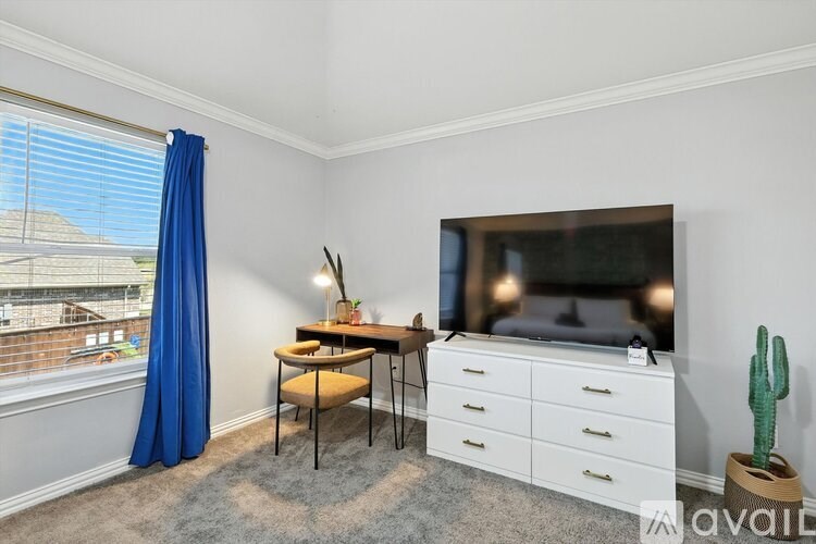 A living room with a blue curtain, a wooden table, a white dresser, and a flat-screen TV.