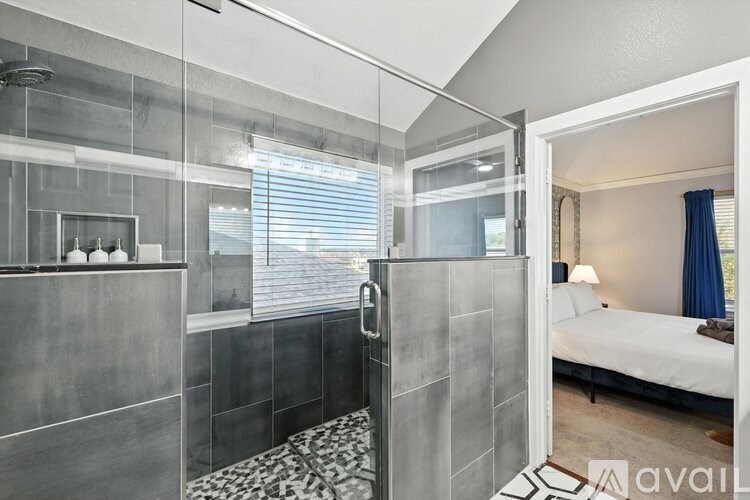 A modern bathroom with a walk-in shower and a glass door leading to a bedroom.