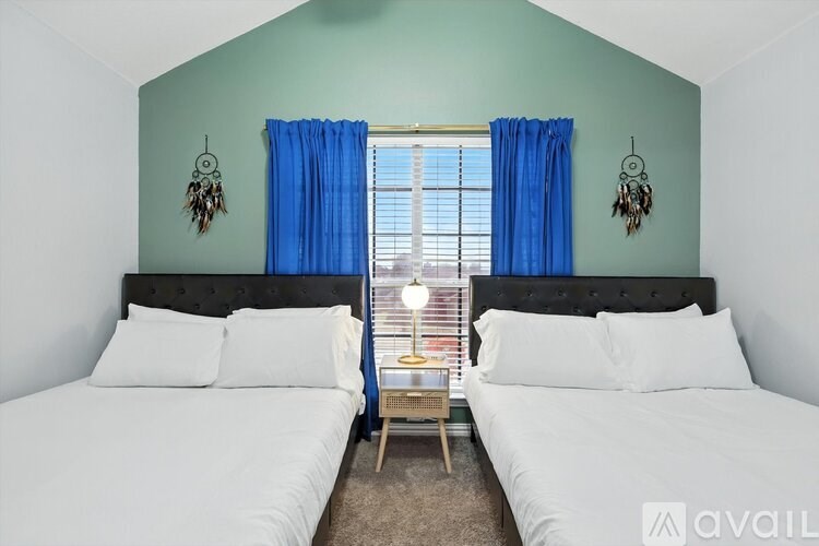 A bedroom with two beds, one with blue curtains, and a dream catcher hanging on the wall.