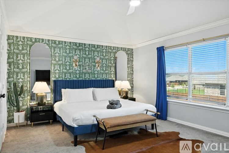 A bedroom with a blue headboard bed, a wooden bench, and a cactus plant on the nightstand.