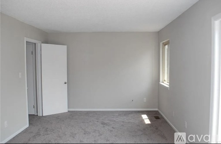 A room with a carpeted floor, a white door, and a window with a white frame.