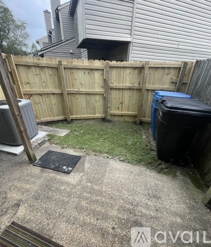 A backyard with a wooden fence, a trash can, and a small patch of grass.
