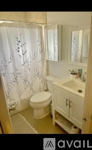 A white toilet in a bathroom with a shower curtain and a sink.