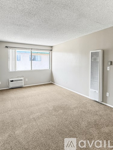 A room with a carpeted floor, a window with blinds, and a wall-mounted air conditioning unit.